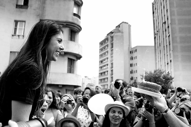 Our small party. Mariana Orsi (left), participants enjoying and photographing (background) and the cake given to Mari (right). I like this photograph. In my opinion, it shows the will, happiness, involvement and the care that the participants have with Click a Pé. Somebody even brought a cake for the birthday. This photograph was taken by Edmilson Silva.