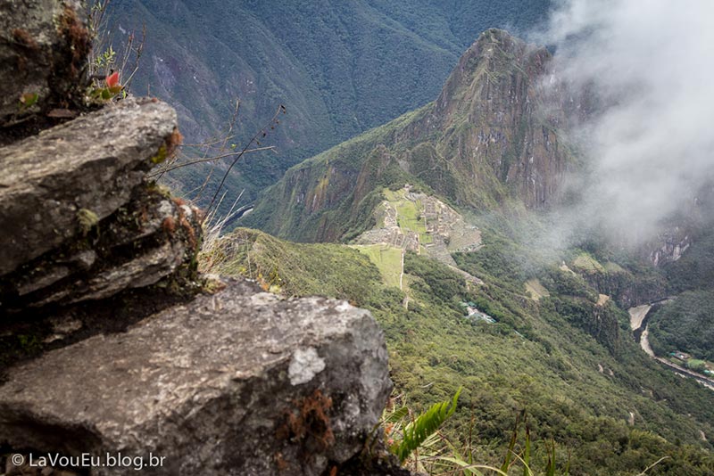 Vista da cidadela e Huayna Picchu próximo ao topo da Montanha Machu Picchu. A sensação no decorrer da subida é muito clara que a cidadela vai ficando distante e cada vez menor. Chega a ser impresseionante a diferença que faz conforme vamos ficando mais alto. Repare como a cidadela está pequena devido à distância/altitude. As pedras na imagem são os degraus desse trecho da subida. Vista da cidadela e Huayna Picchu próximo ao topo da Montanha Machu Picchu. A sensação no decorrer da subida é muito clara que a cidadela vai ficando distante e cada vez menor. Chega a ser impresseionante a diferença que faz conforme vamos ficando mais alto. Repare como a cidadela está pequena devido à distância/altitude. As pedras na imagem são os degraus desse trecho da subida.